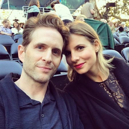 Glenn Howerton in a black t-shirt and coat poses a picture with wife Jill Latiano.